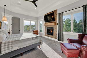 Carpeted bedroom with a large fireplace, a raised ceiling, ceiling fan, and wood ceiling