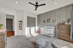 Carpeted bedroom with a ceiling fan, a crib, a decorative wall, and a closet
