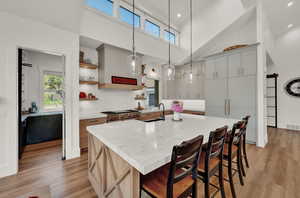 Kitchen featuring a towering ceiling, open shelves, a breakfast bar, a spacious island, and light wood-style floors