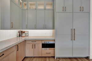 Kitchen featuring light brown cabinets, glass insert cabinets, light wood-type flooring, and stainless steel microwave