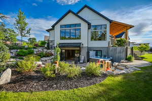 Back of property with a hot tub, a patio area, a balcony, a lawn, and board and batten siding