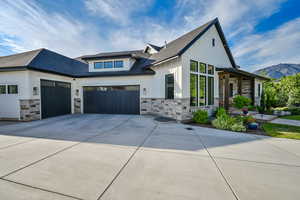 Modern farmhouse style home featuring stone siding, board and batten siding, concrete driveway, roof with shingles, and a garage