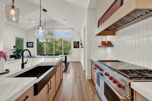 Kitchen featuring range with two ovens, light stone counters, custom exhaust hood, pendant lighting, and vaulted ceiling
