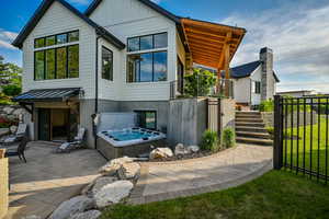 Rear view of property with a hot tub, a patio area, stairway, board and batten siding, and a gate