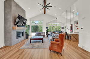 Living area with beamed ceiling, a tile fireplace, high vaulted ceiling, light wood-style flooring, and a ceiling fan