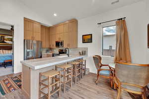 Kitchen featuring light brown cabinets, a kitchen breakfast bar, vaulted ceiling, appliances with stainless steel finishes, and light wood-style flooring