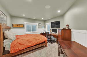 Bedroom with a wainscoted wall, light colored carpet, an office area, and recessed lighting