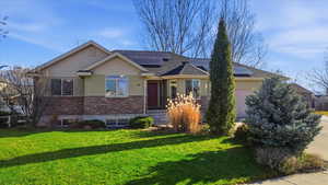 View of front of property with roof mounted solar panels, a front yard, a garage, roof with shingles, and stone siding