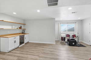 Indoor wet bar with open shelves, white cabinets, recessed lighting, light wood finished floors, and beverage cooler