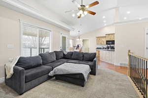Living area featuring vaulted ceiling, a chandelier, a ceiling fan, and crown molding