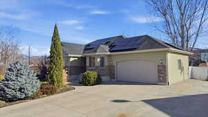 View of front of property with concrete driveway, roof mounted solar panels, stone siding, and an attached garage