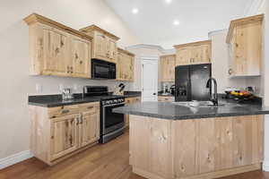 Kitchen with light brown cabinets, black appliances, dark countertops, a peninsula, and lofted ceiling