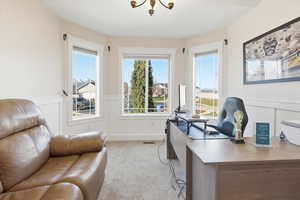 Home office featuring a decorative wall, a wainscoted wall, healthy amount of natural light, light colored carpet, and a chandelier