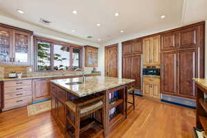 Kitchen featuring glass insert cabinets, light stone counters, paneled fridge, light wood-type flooring, and recessed lighting