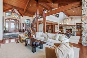 Living area featuring a chandelier, hardwood / wood-style flooring, high vaulted ceiling, stairway, and a stone fireplace