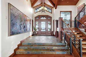 Foyer featuring stone tile flooring, a chandelier, high vaulted ceiling, stairs, and a wooden ceiling with exposed beams