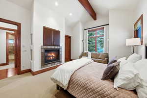 Bedroom with light colored carpet, a glass covered fireplace, and recessed lighting