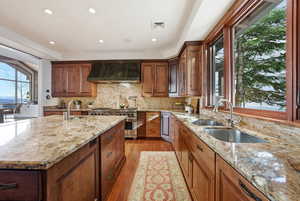 Kitchen featuring light stone counters, decorative backsplash, light wood-style floors, recessed lighting, and a center island with sink