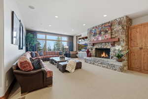 Carpeted living room with a stone fireplace and recessed lighting