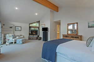 Carpeted bedroom featuring a stone fireplace, beam ceiling, and high vaulted ceiling