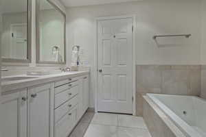 Bathroom featuring double vanity, light tile patterned floors, and a jetted tub