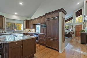 Kitchen with built in appliances, light stone countertops, light wood finished floors, tasteful backsplash, and high vaulted ceiling