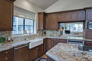 Kitchen featuring light stone counters, lofted ceiling, appliances with stainless steel finishes, tasteful backsplash, and healthy amount of natural light