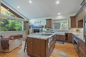 Kitchen featuring open floor plan, vaulted ceiling, light stone counters, a breakfast bar, and decorative backsplash