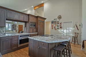 Kitchen with built in appliances, a center island, light wood-style flooring, light stone countertops, and high vaulted ceiling