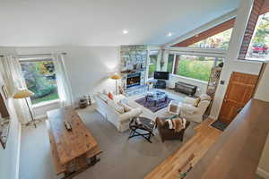 Living room featuring a stone fireplace, healthy amount of natural light, high vaulted ceiling, and light wood-type flooring