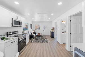 Kitchen with stainless steel appliances, white cabinets, light wood finished floors, recessed lighting, and open floor plan