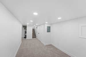 Hallway with recessed lighting, light colored carpet, stairs, electric panel, and electric water heater