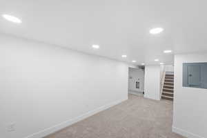 Finished basement with recessed lighting, electric panel, stairs, and light colored carpet