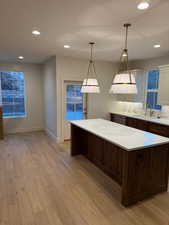 Kitchen with recessed lighting, light wood finished floors, decorative light fixtures, a center island, and dark brown cabinets