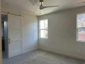 Unfurnished bedroom with a barn door, carpet flooring, and a ceiling fan