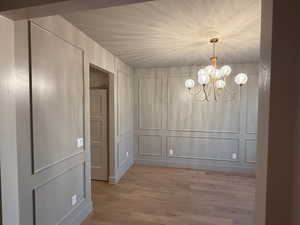 Unfurnished dining area with a decorative wall, a chandelier, and light wood-type flooring