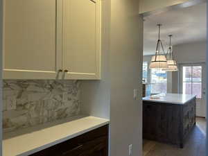 Kitchen with tasteful backsplash, a center island, pendant lighting, white cabinetry, and wood finished floors