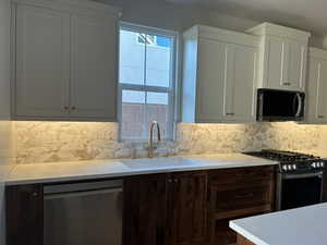 Kitchen with stainless steel appliances, backsplash, light stone countertops, and white cabinetry