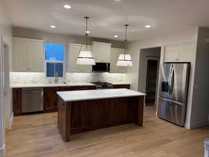 Kitchen with stainless steel appliances, hanging light fixtures, white cabinetry, a center island, and light wood finished floors