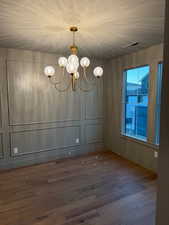 Unfurnished dining area featuring dark wood-type flooring, a chandelier, and a decorative wall