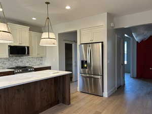 Kitchen with appliances with stainless steel finishes, decorative light fixtures, backsplash, light wood-style flooring, and recessed lighting