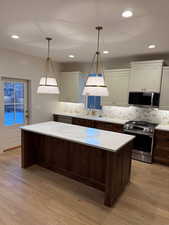 Kitchen featuring appliances with stainless steel finishes, light wood-style floors, a center island, pendant lighting, and white cabinets