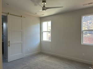 Unfurnished bedroom featuring a barn door, carpet flooring, and a ceiling fan