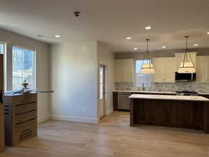 Kitchen with light countertops, white cabinets, healthy amount of natural light, light wood-style floors, and recessed lighting