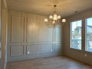 Unfurnished dining area with a decorative wall, a chandelier, and light wood finished floors