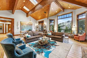 Living area with high vaulted ceiling, a wood ceiling with exposed beams, recessed lighting, a chandelier, and a skylight