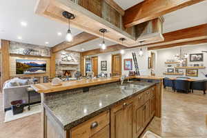 Kitchen with open floor plan, hanging light fixtures, brown cabinets, a kitchen island with sink, and beam ceiling