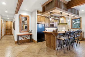 Kitchen with brown cabinetry, freestanding refrigerator, custom range hood, a breakfast bar, and a kitchen island