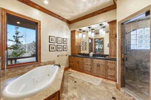 Full bathroom with double vanity, healthy amount of natural light, a jetted tub, a shower stall, and ornamental molding