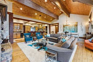 Living room featuring light wood-style flooring, a wood ceiling with exposed beams, a chandelier, wine cooler, and high vaulted ceiling